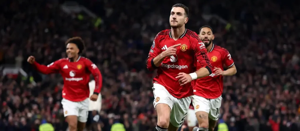 Diogo Dalot pointing to Manchester United's badge