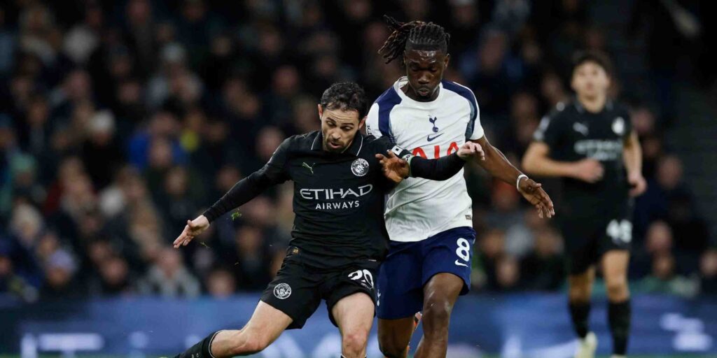 Bernardo Silva trying to pass the ball under pressure from a Tottenham player