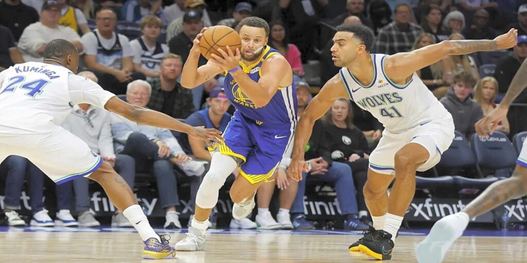 Steph Curry dribbling the ball between two Minnesota Timberwolves players